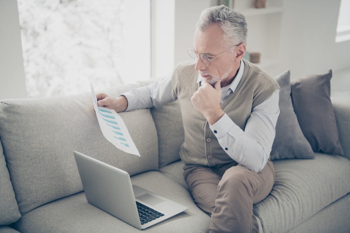 Mature man reviewing investment stats on laptop at home